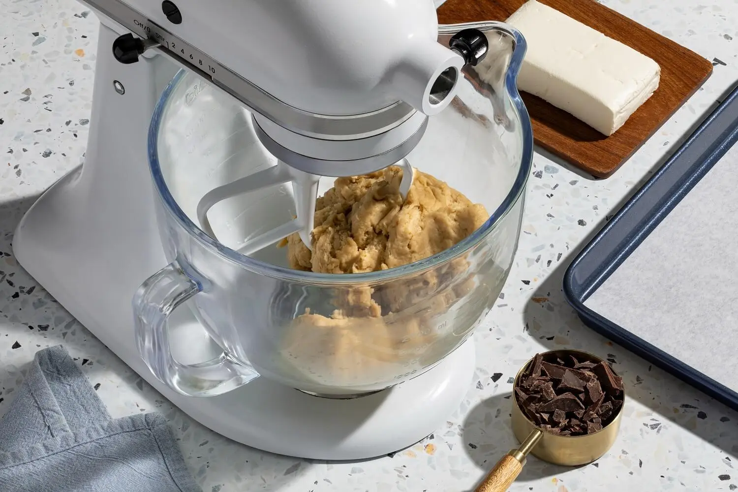 A mixer with flour, cornstarch, baking soda, and salt, along with a cup of chocolate chunks.
