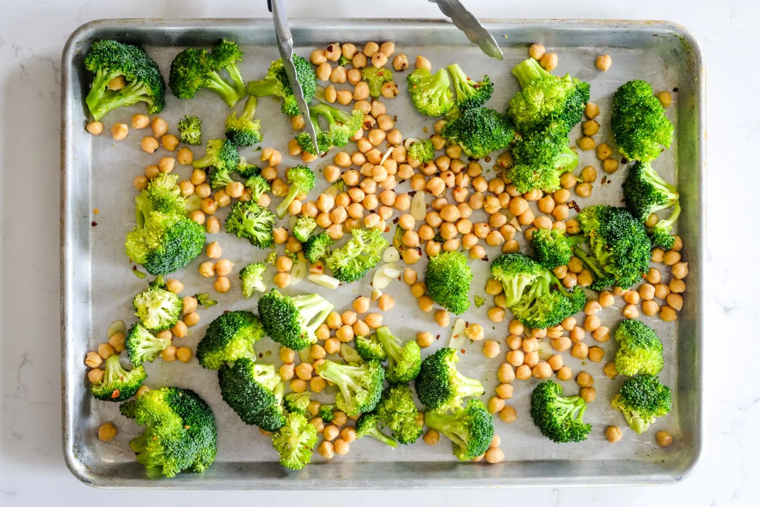 Broccoli and chickpeas on a baking sheet tossed in garlic, oil, and red-pepper flakes