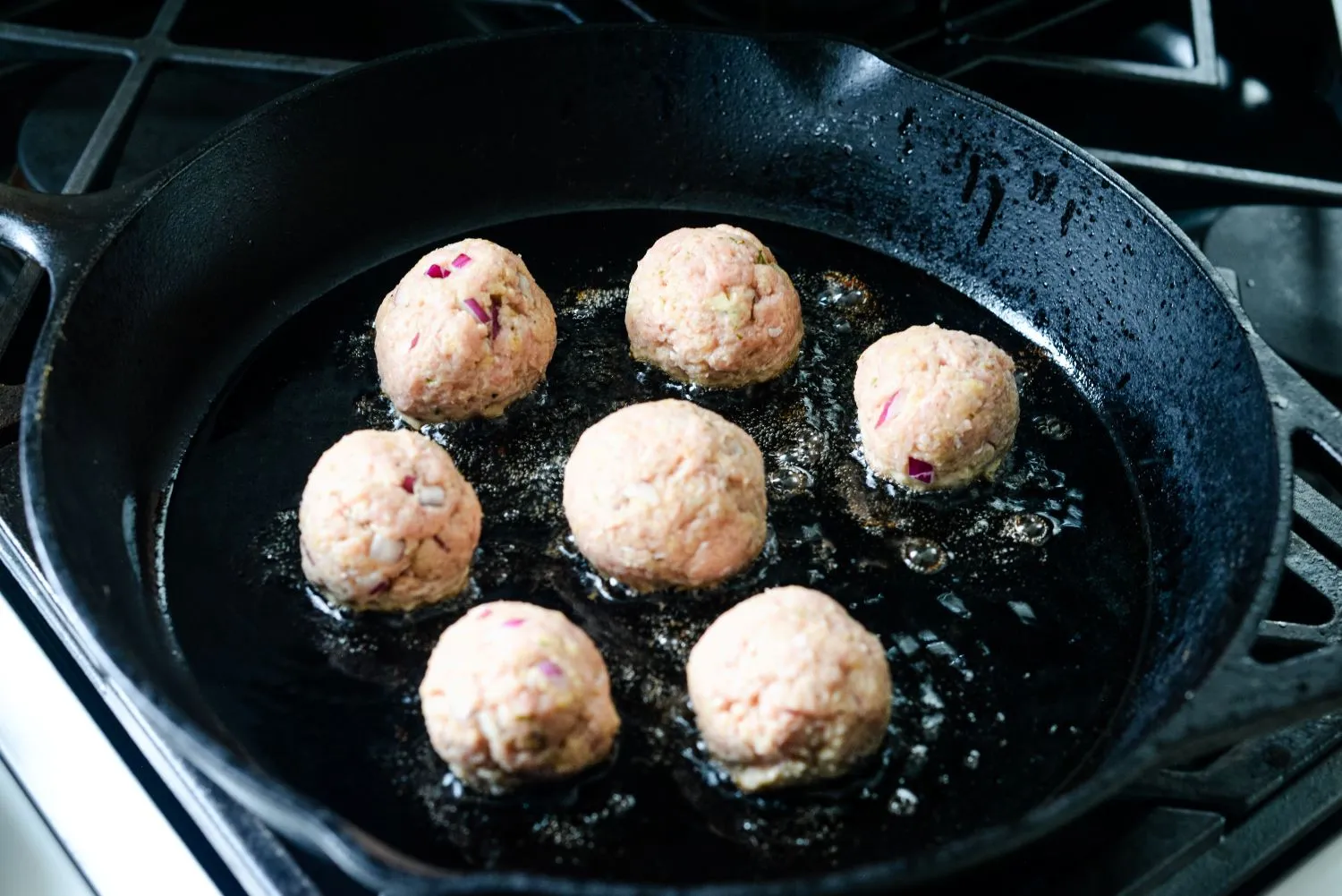 Six meatballs cooked in a skilled with olive oil.