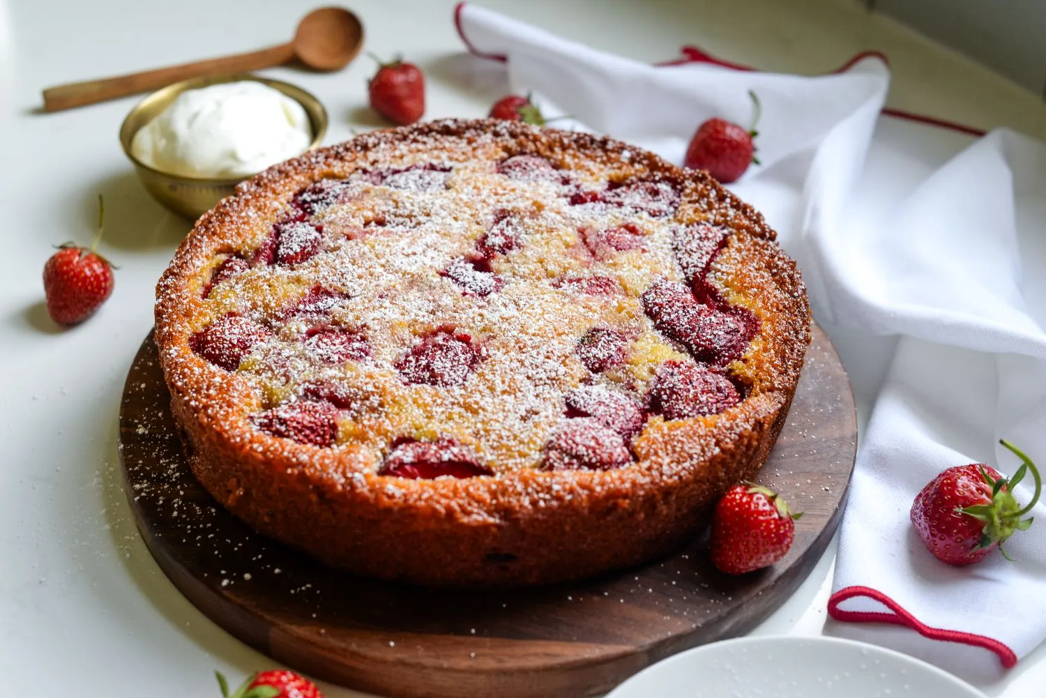 A lemon berry yogurt cake on a cake platter, topped with strawberries and confectioners' sugar.