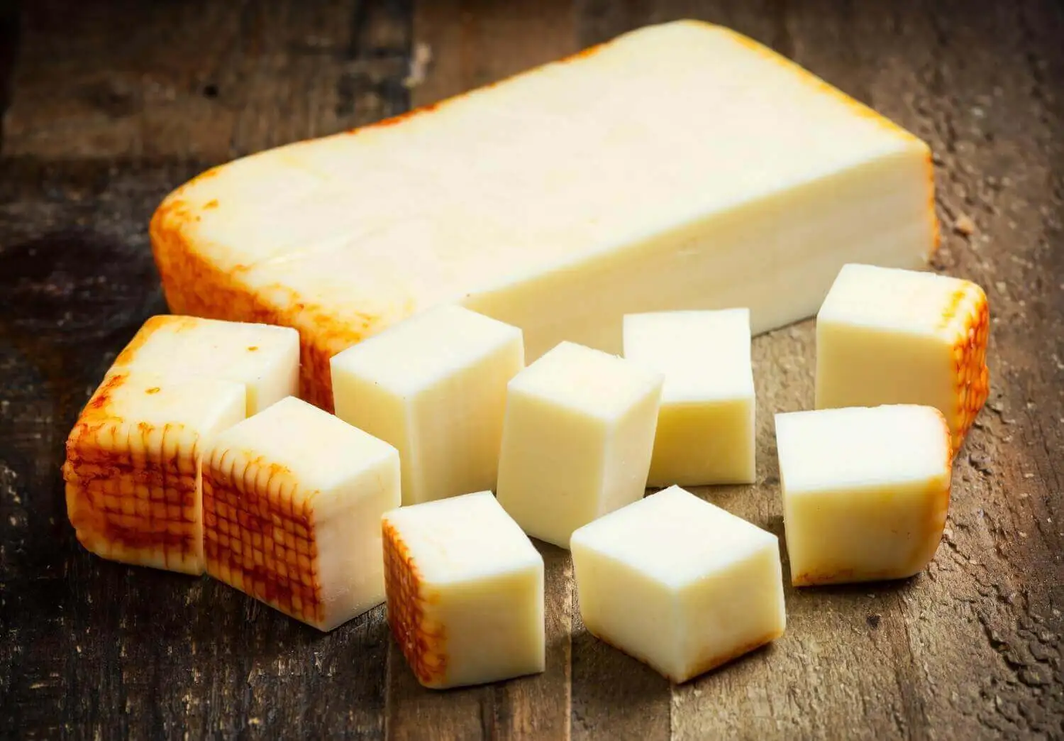 Block and cubes of Muenster cheese on wood background