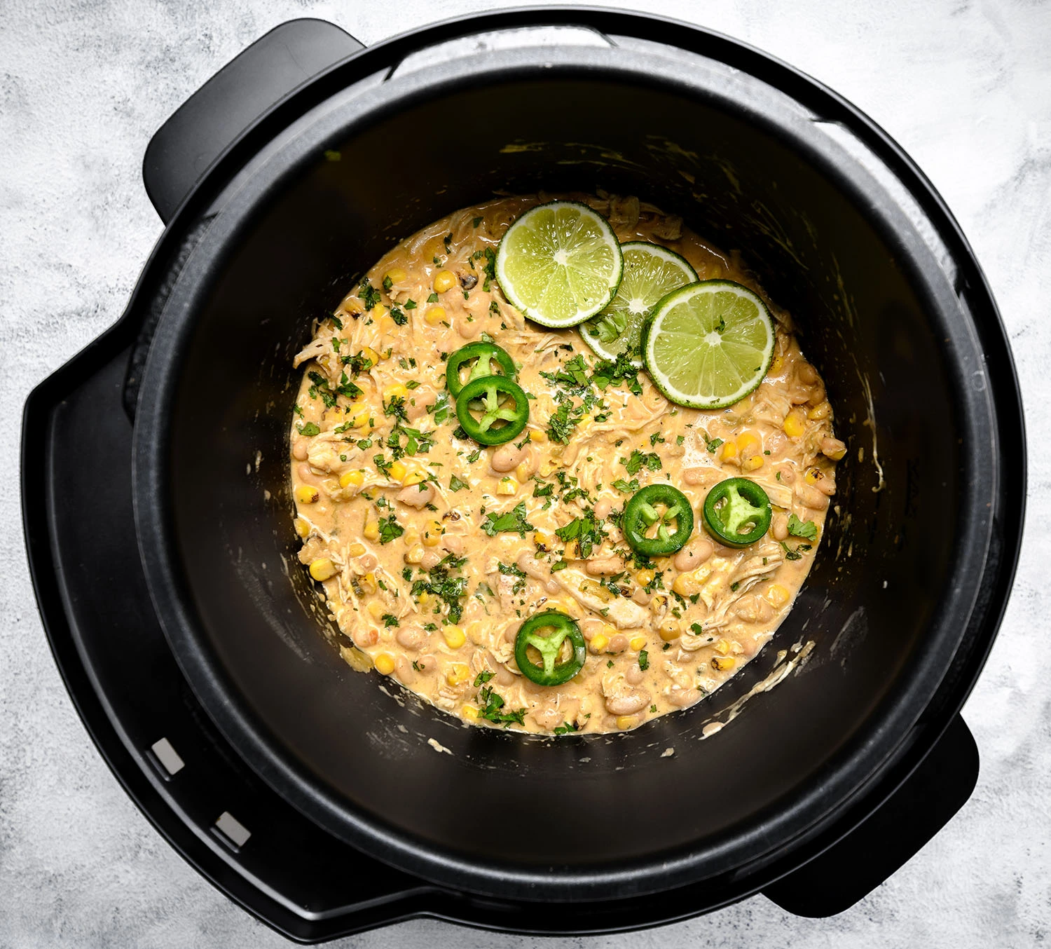 white chicken chili in a pressure cooker topped with jalapeños and sliced limes.