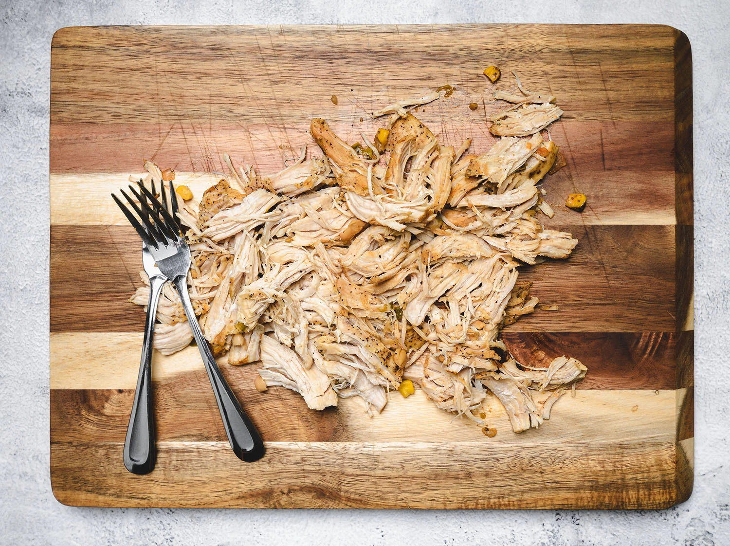 Chicken shredded using forks on a cutting board.