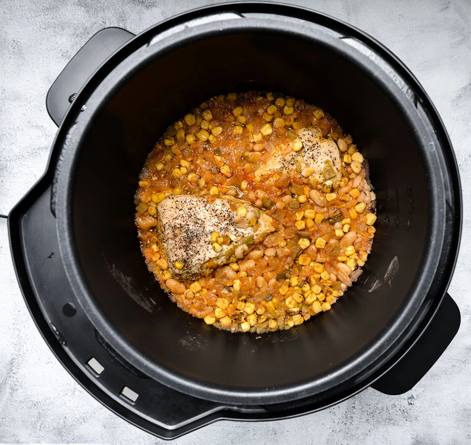Ingredients for white bean chicken chilli in a pressure cooker, including white beans, chicken breast, corn, and green chiles.
