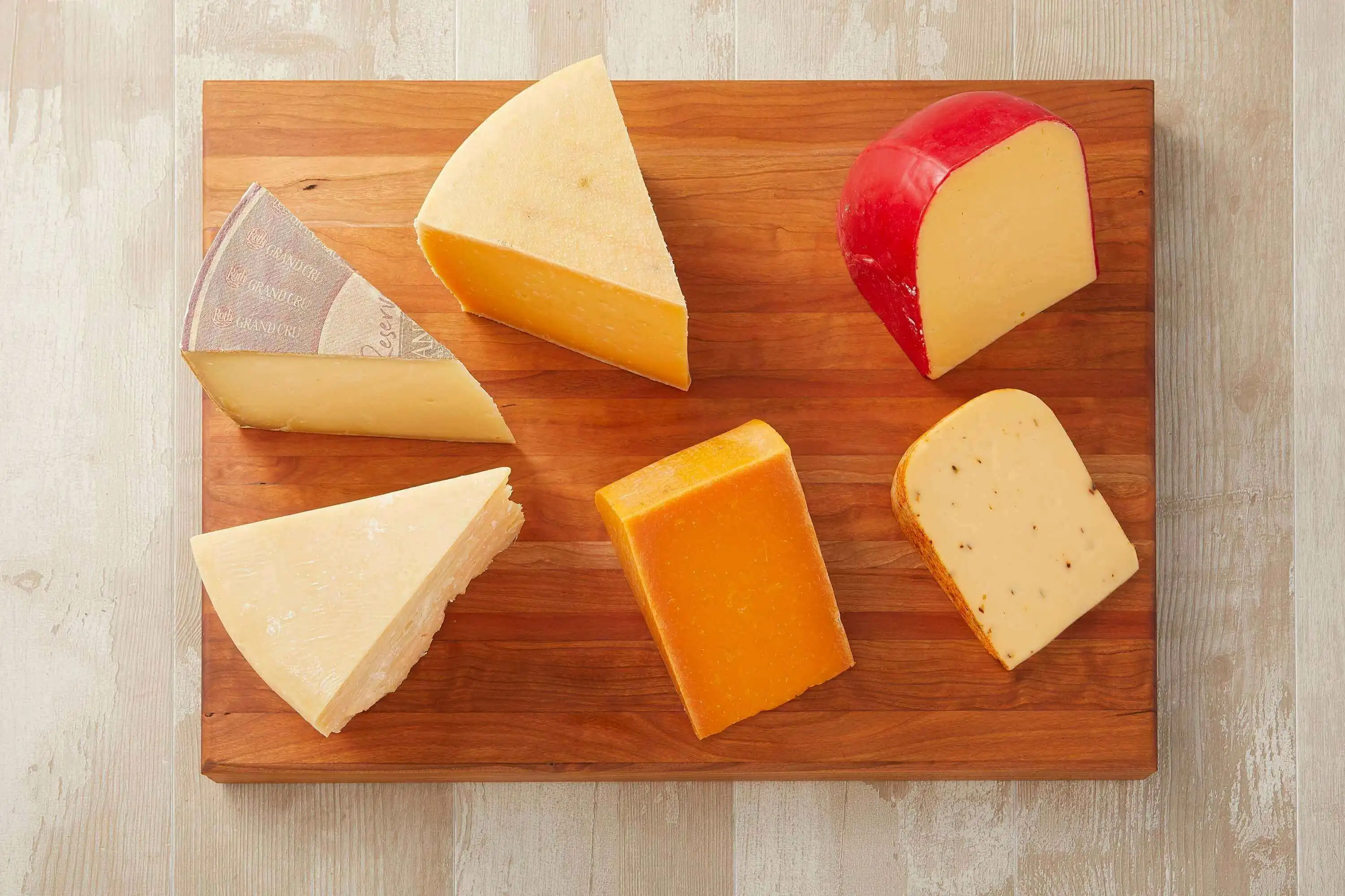 Wooden cheese board with a wide selection of cheeses, including creamy brie, cheddar, nutty gouda, and havarti.
