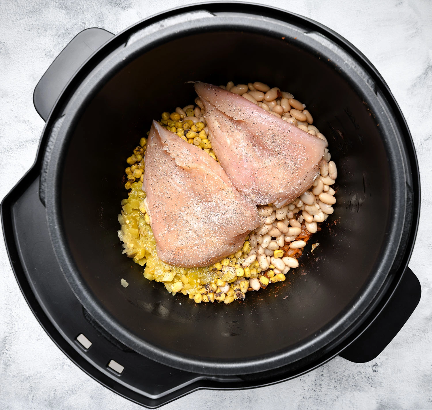 Canned beans, frozen corn, green chiles, and chicken breast in a pressure cooker.