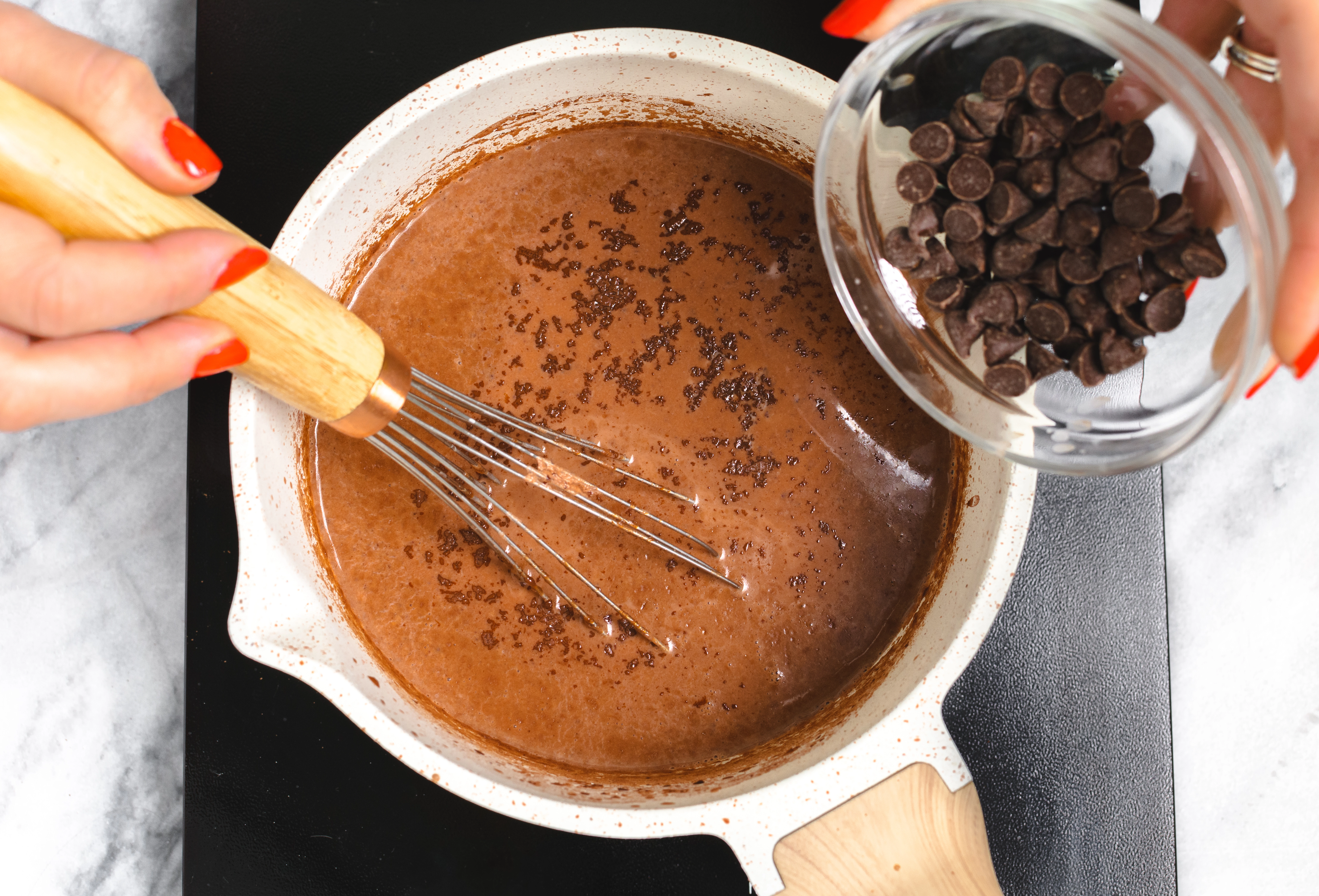 A pot of cocoa powder, milk, vanilla extract, and chocolate chips whisked together on the stovetop.