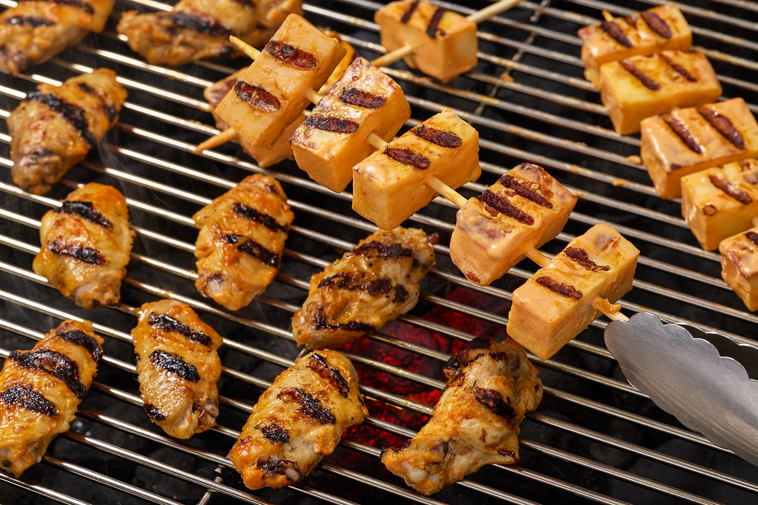 Grilling chicken wings and halloumi skewers with charred grill marks.