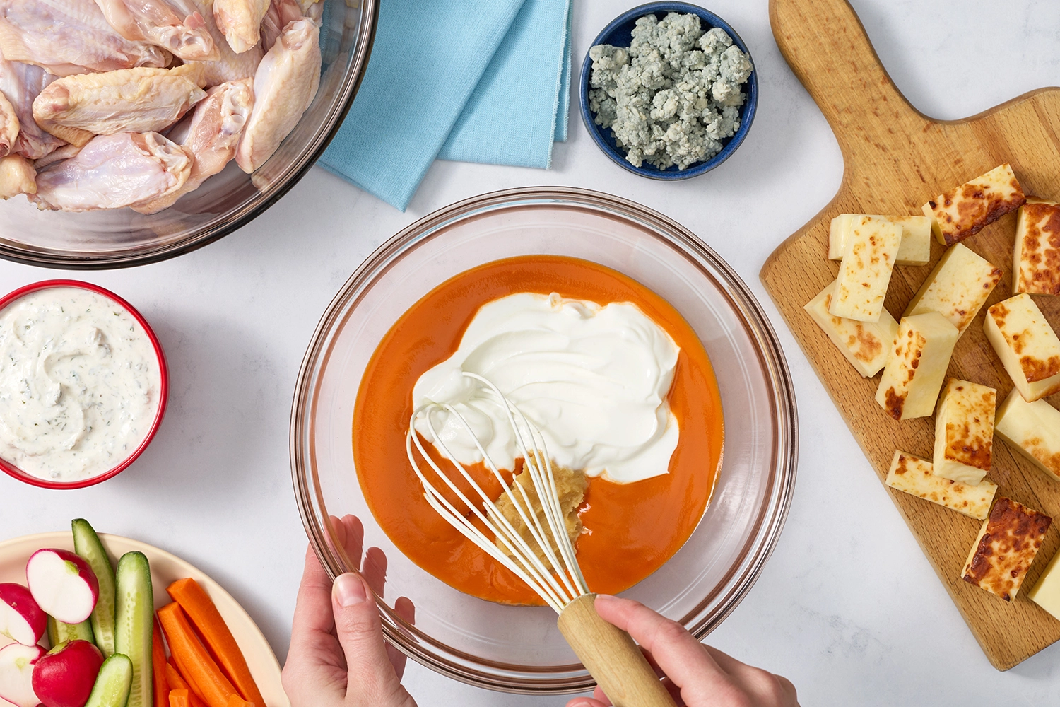 Whisking miso buffalo sauce in a bowl with raw wings and halloumi nearby.