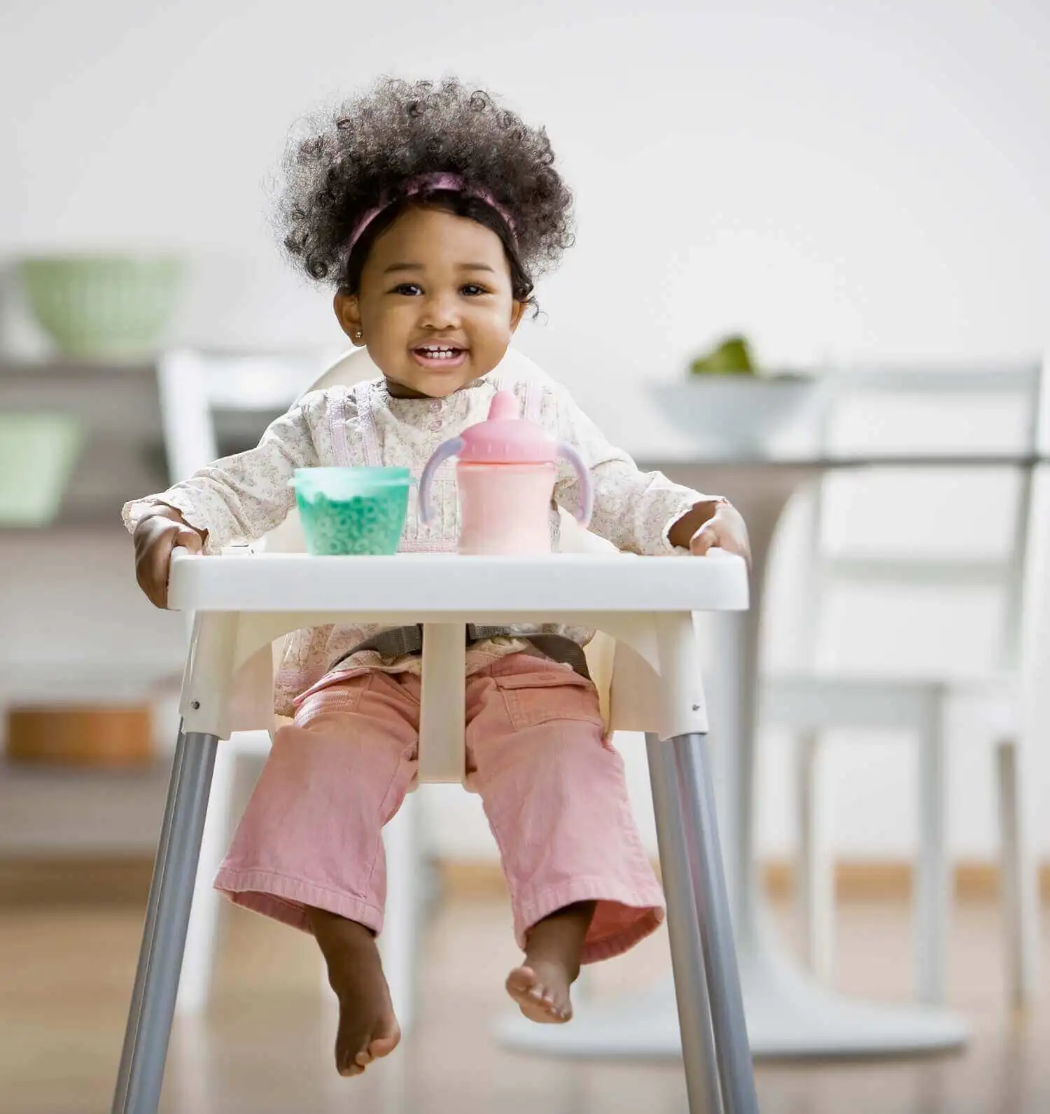 A toddler sitting in a high chair with cereal and milk on the table.