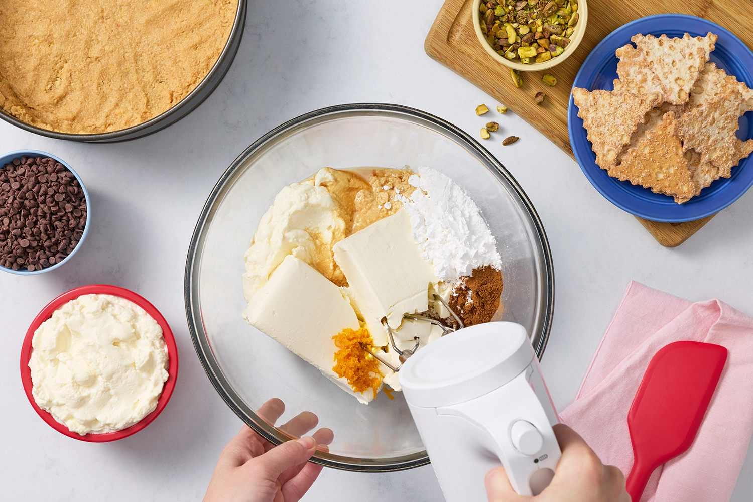 Mixing cream cheese, ricotta, and orange zest in a glass bowl.