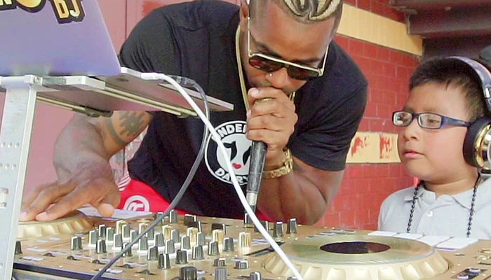 A DJ explaining the controls on a mixer to a kid.