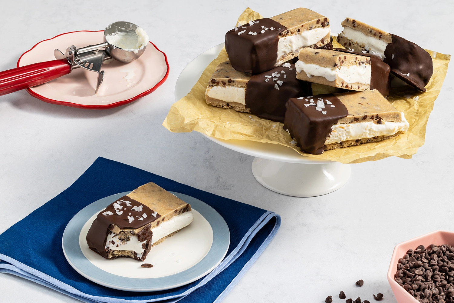 Chocolate-dipped cookie dough ice cream sandwiches with one bitten sandwich on a plate.