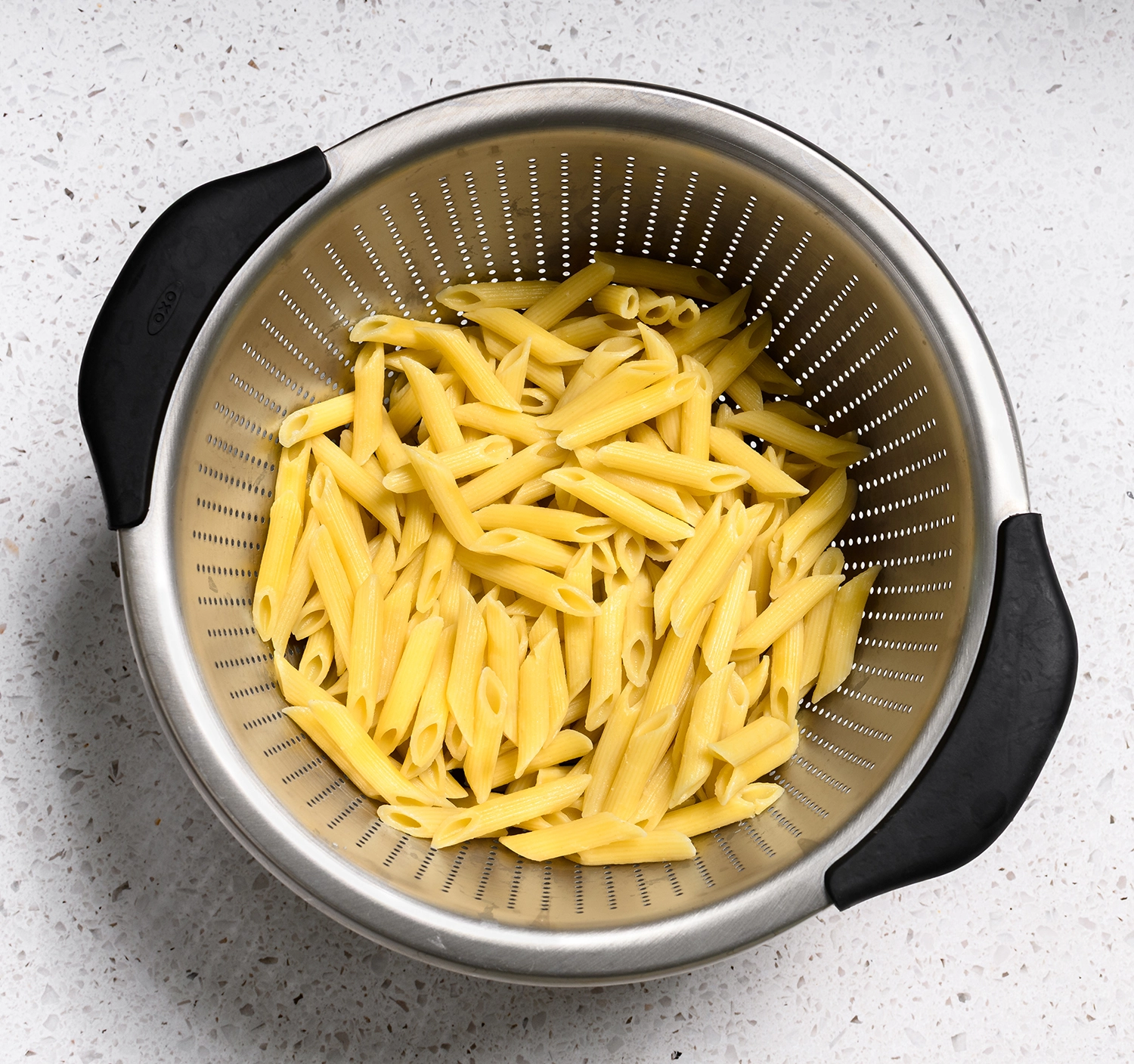 One pound of penne pasta cooked and drained in a strainer.
