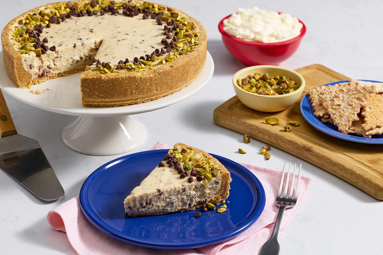 Sliced cannoli cheesecake topped with mini chocolate chips and crushed pistachios.