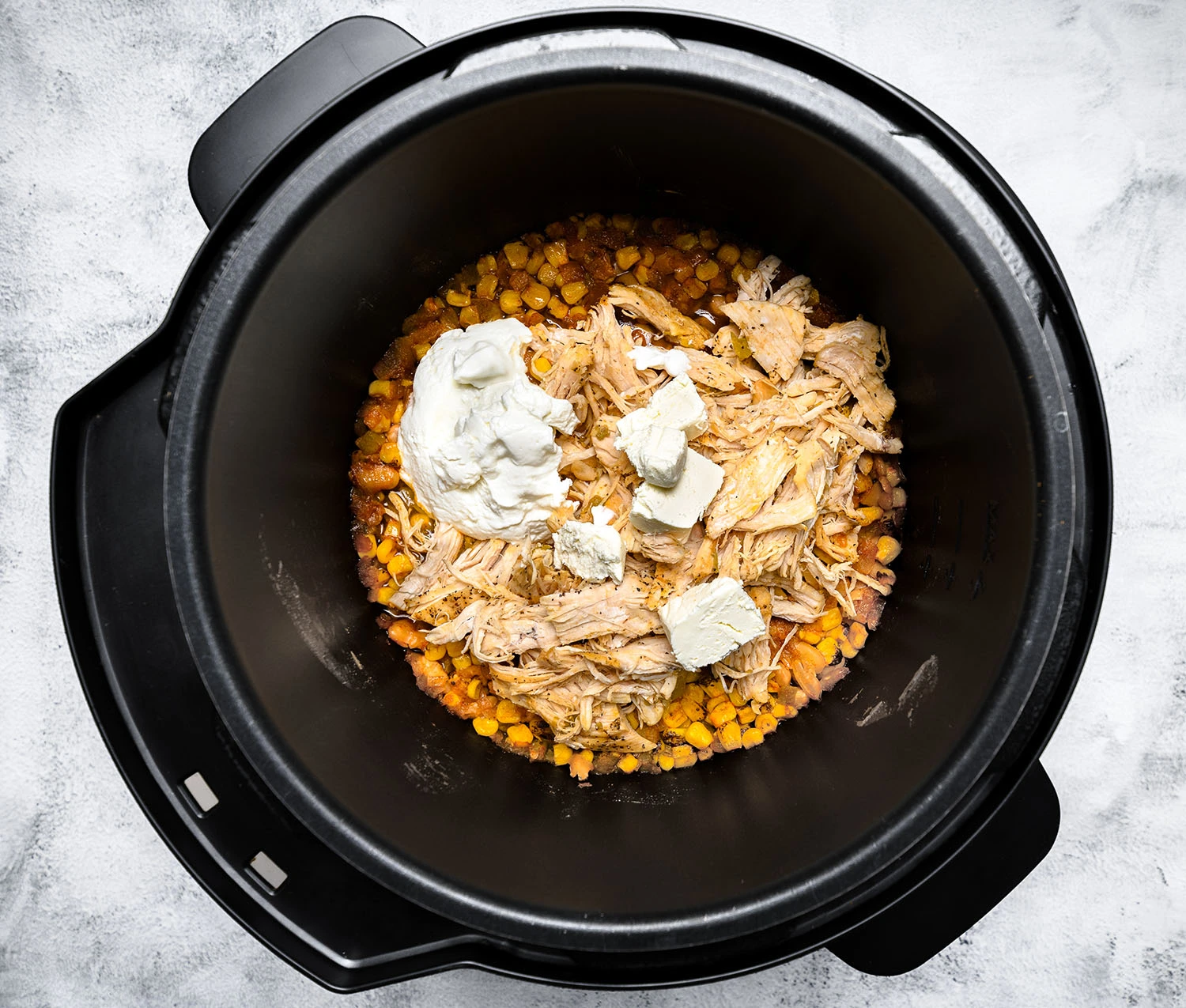 Ingredients for a white chicken chili including shredded chicken and Greek yogurt, in a pressure cooker.