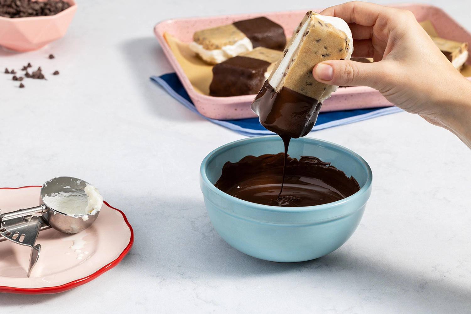 Hand dipping a cookie dough ice cream sandwich into a bowl of melted dark chocolate.