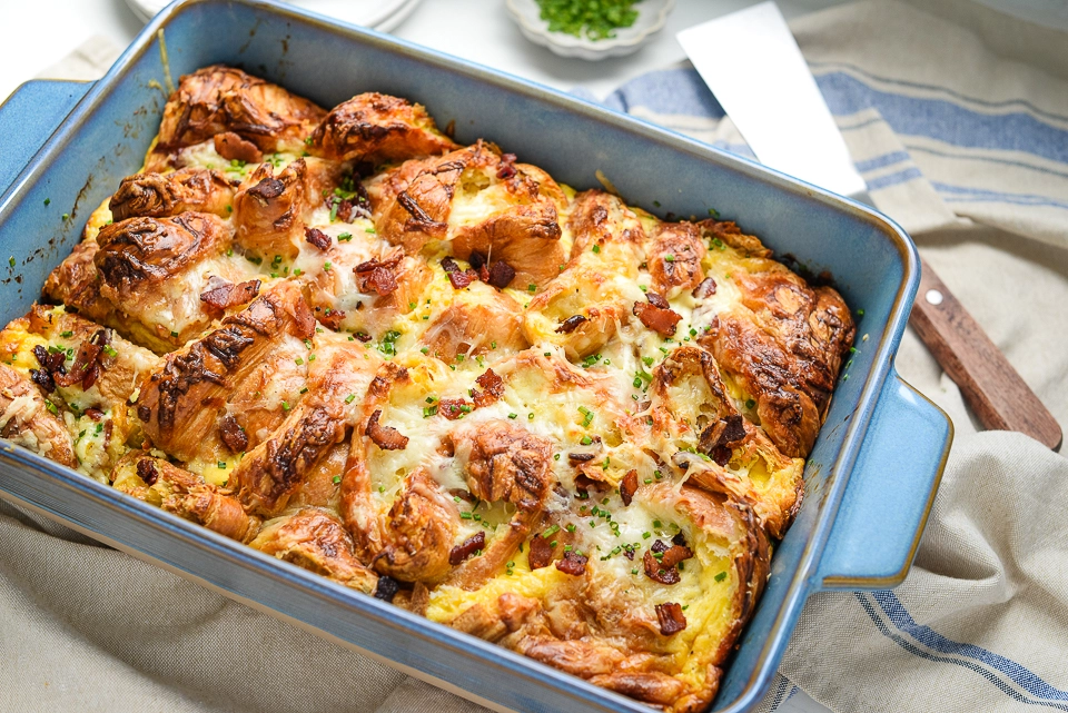 A spatula lifting a portion out of the blue baking dish filled with baked croissant casserole.