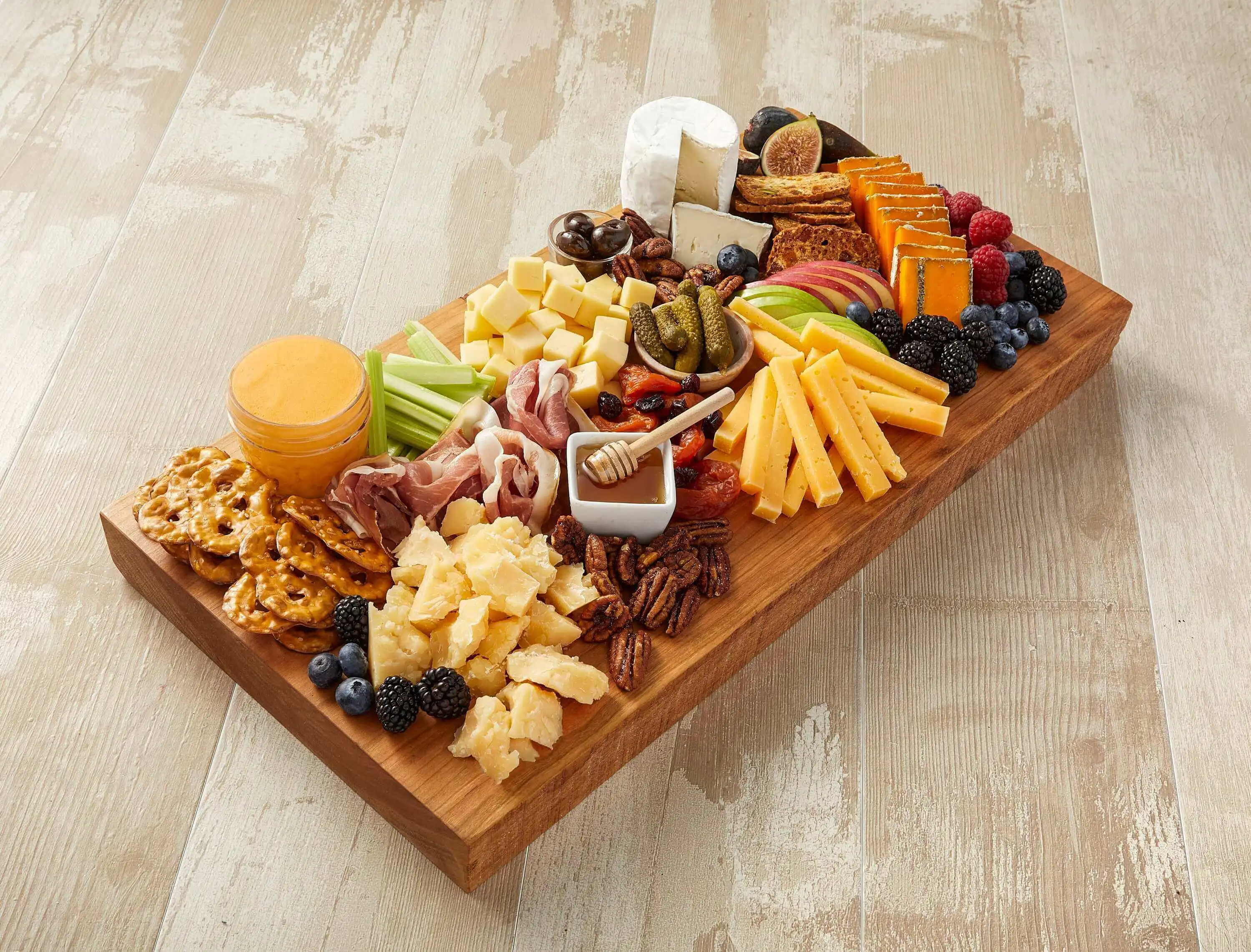 An elegant cheese board with a diverse selection of cheeses, fresh and dried fruits, cured meats, vegetables, and crackers