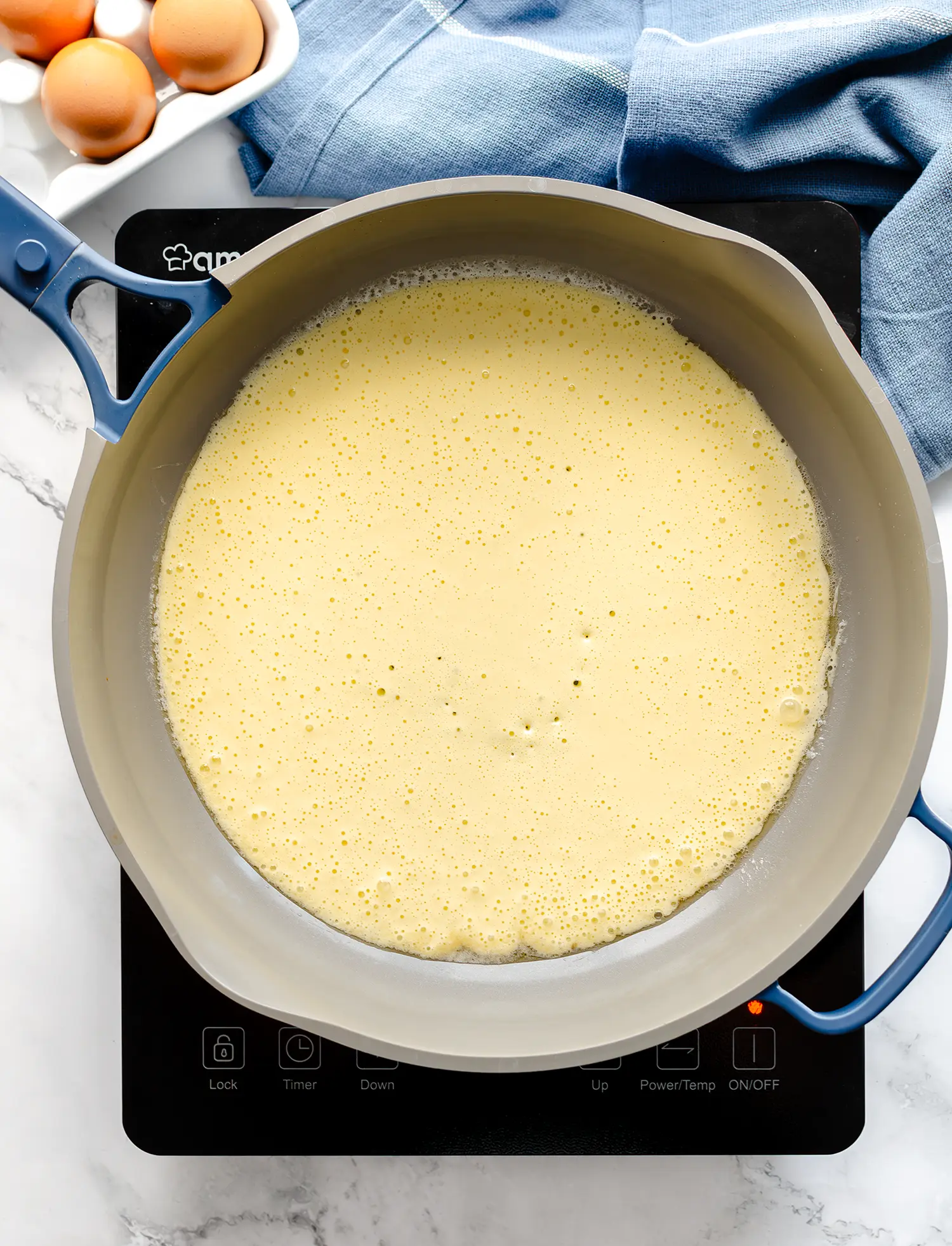 A hot skillet containing a seasoned blend of eggs and cottage cheese cooking on a stovetop.