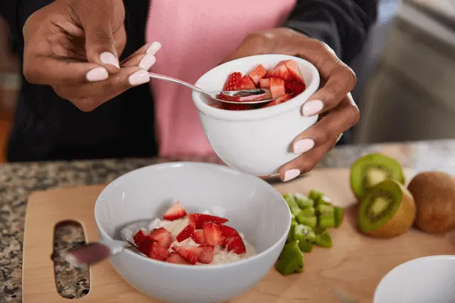 A woman's hands place freshly cut strawberries on a plate of cottage cheese.
