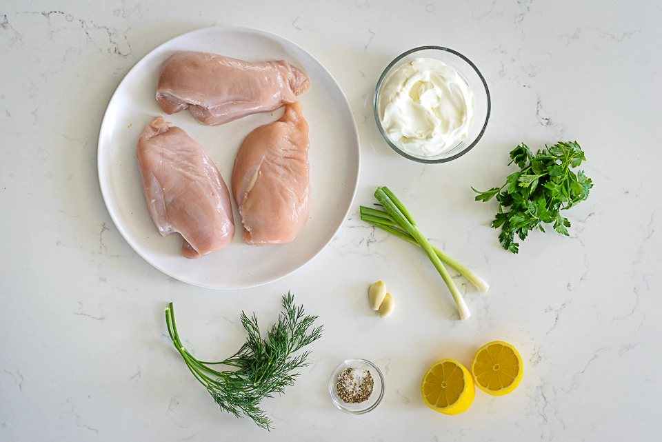 Ingredients for grilled chicken wrap including raw chicken breasts, greek yogurt, herbs, garlic and lemon