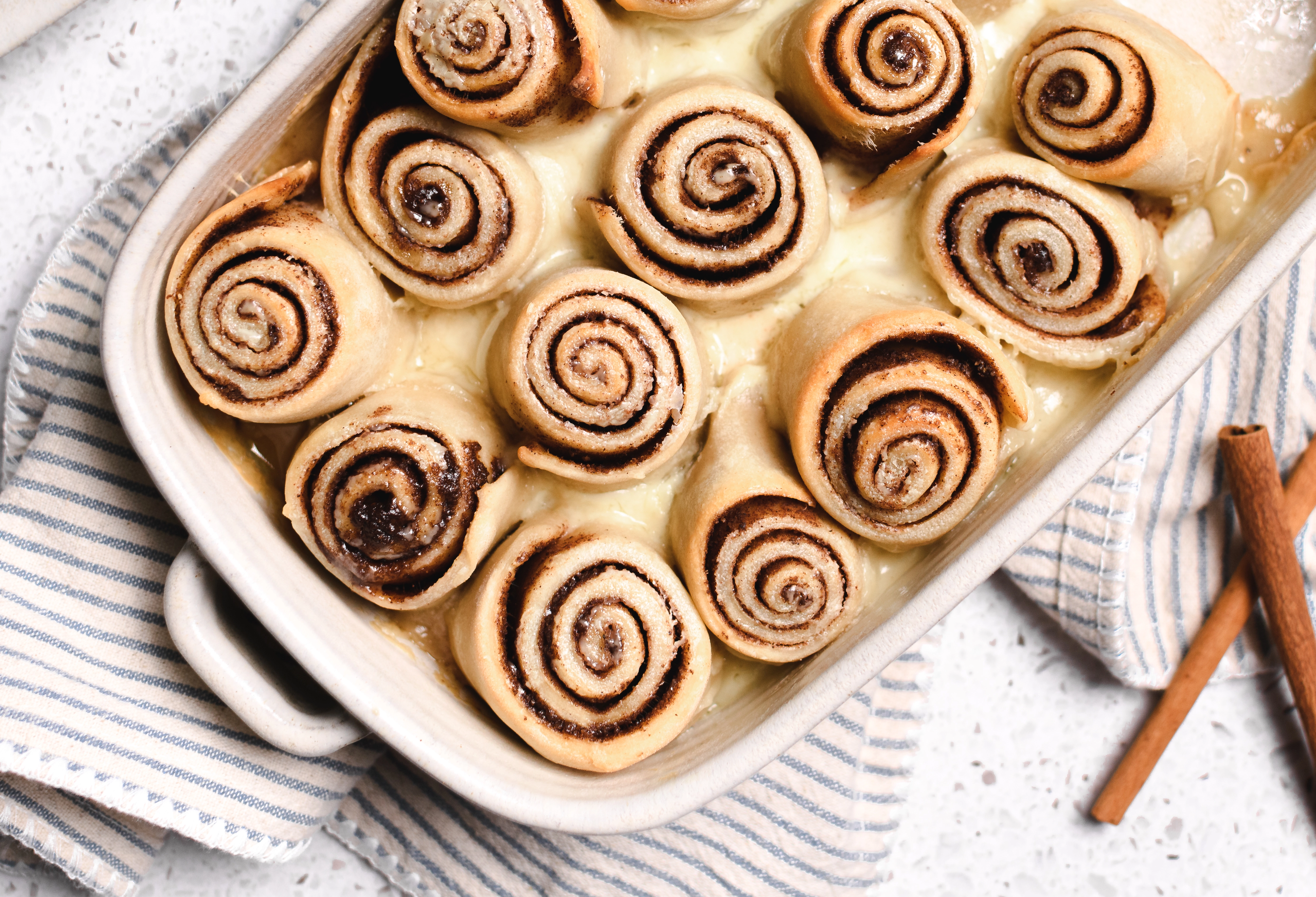 Greek Yogurt Chai Cinnamon Rolls covered in heavy cream in a baking dish.