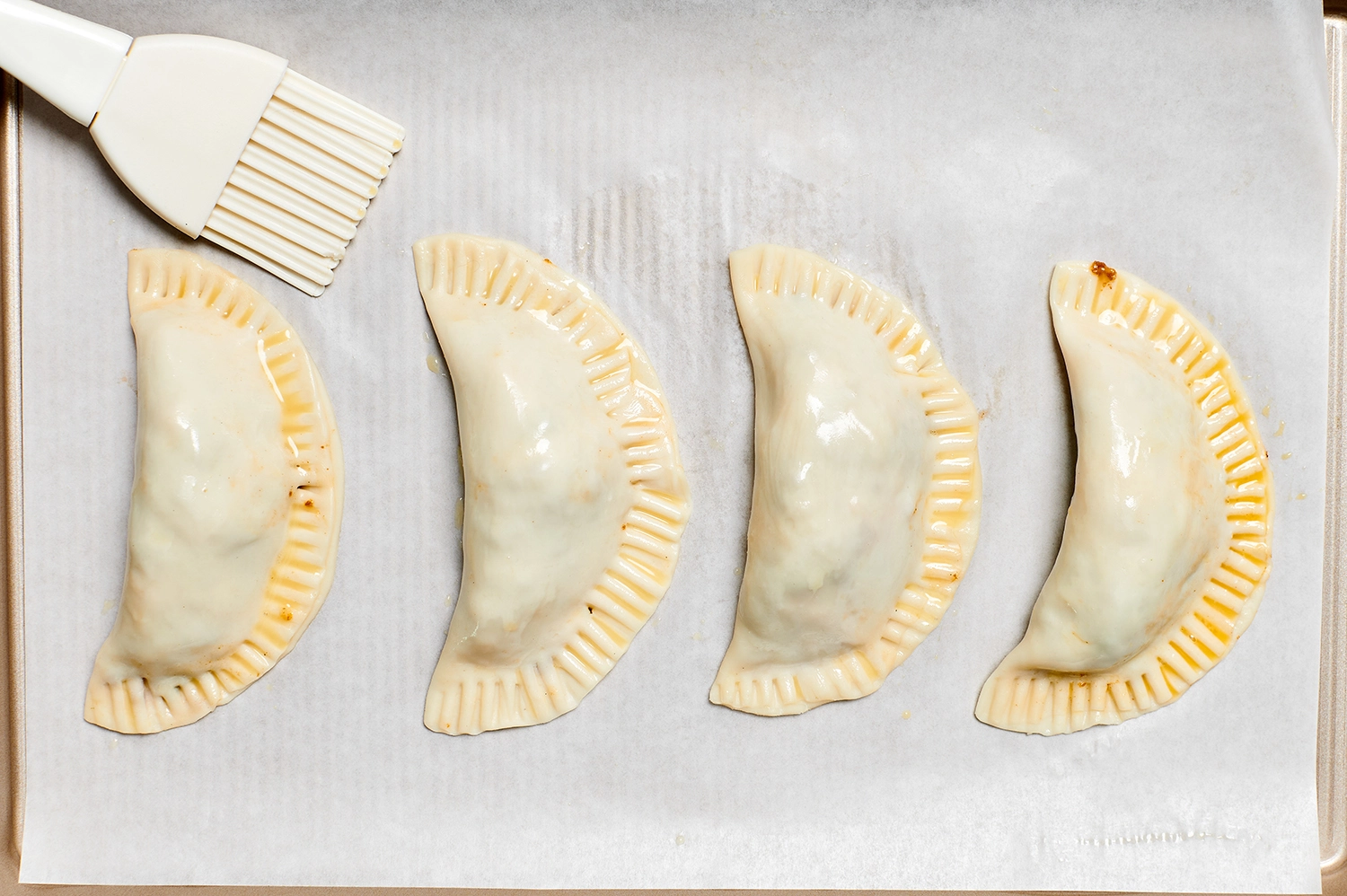 Four assembled empanada filled with queso fundido and chorizo, brushed with egg wash.