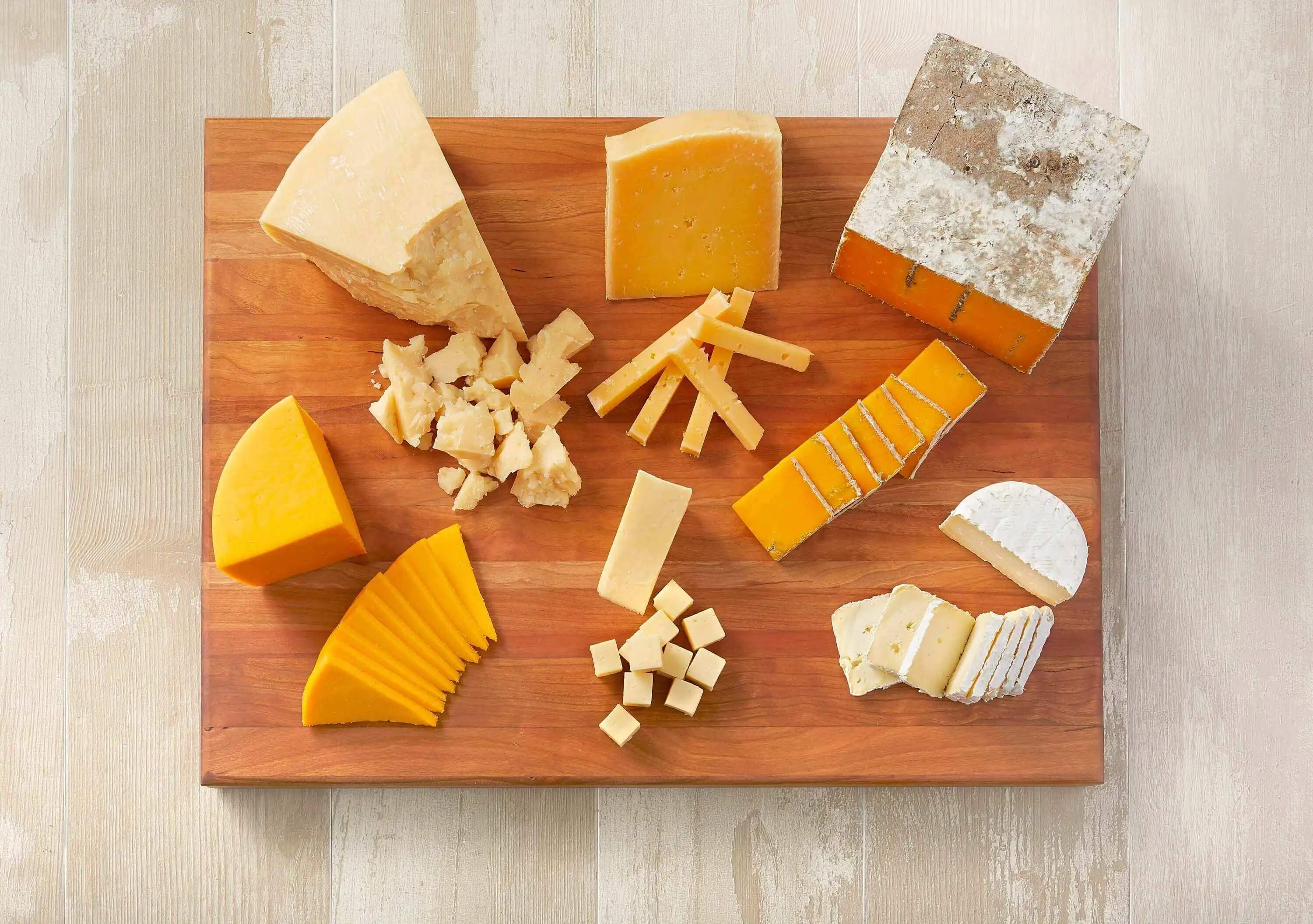 A cheese platter arranged on a wooden table, featuring a diverse selection of cheeses sliced into squares and triangles