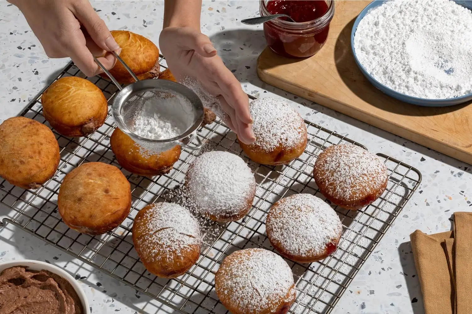 Stuffed sufganiyot sprinkled with powdered sugar on a kitchen rack.