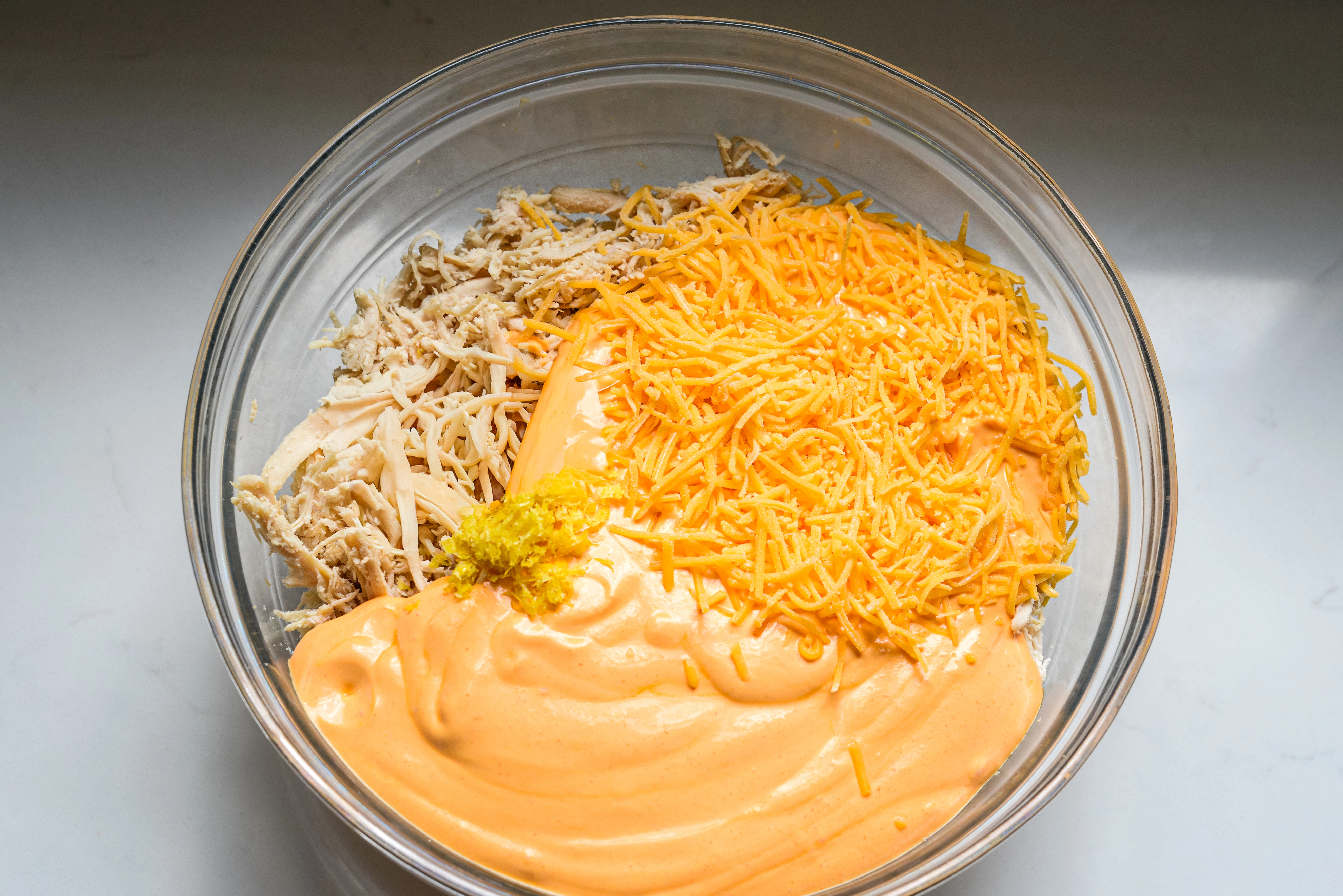 Shredded chicken, cottage cheese mixture, cheddar cheese, and lemon zest in a bowl.