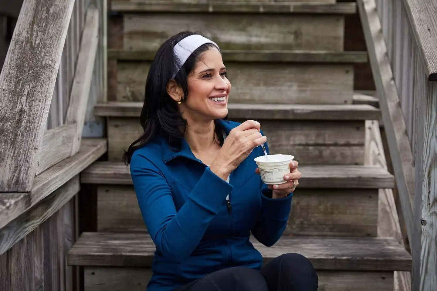 Woman eating cup of yogurt while sitting on staircase.