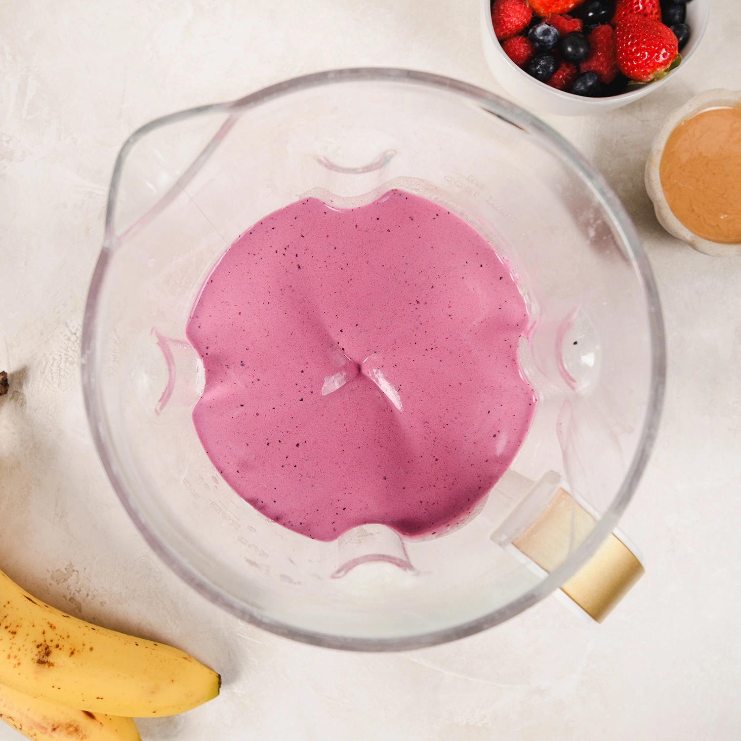 ingredients for a high-protein peanut butter and jelly smoothie blended in a blender.