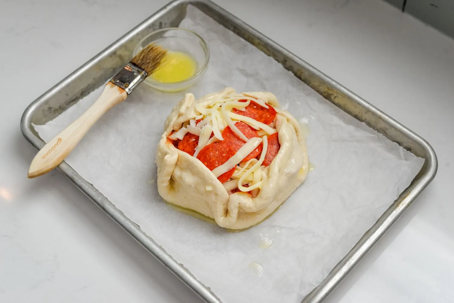 Brie wheel with pinched crust to form a pizza shape, coated in melted butter