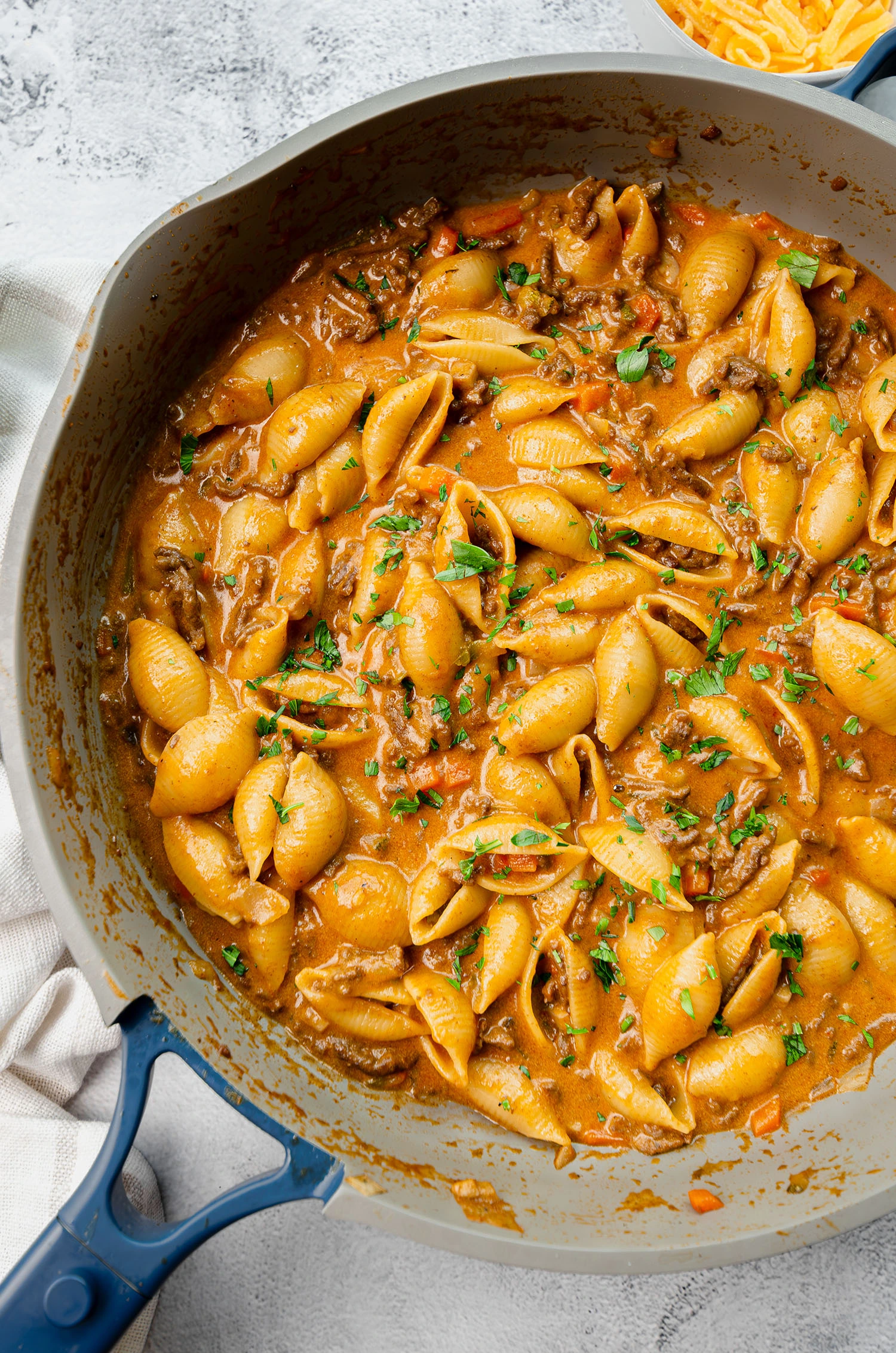 A completed hamburger veggie pasta dish featuring ground beef, carrots, onion, mushroom, zucchini, and cheddar cheese in a pan garnished with fresh parsley, ready to be served.