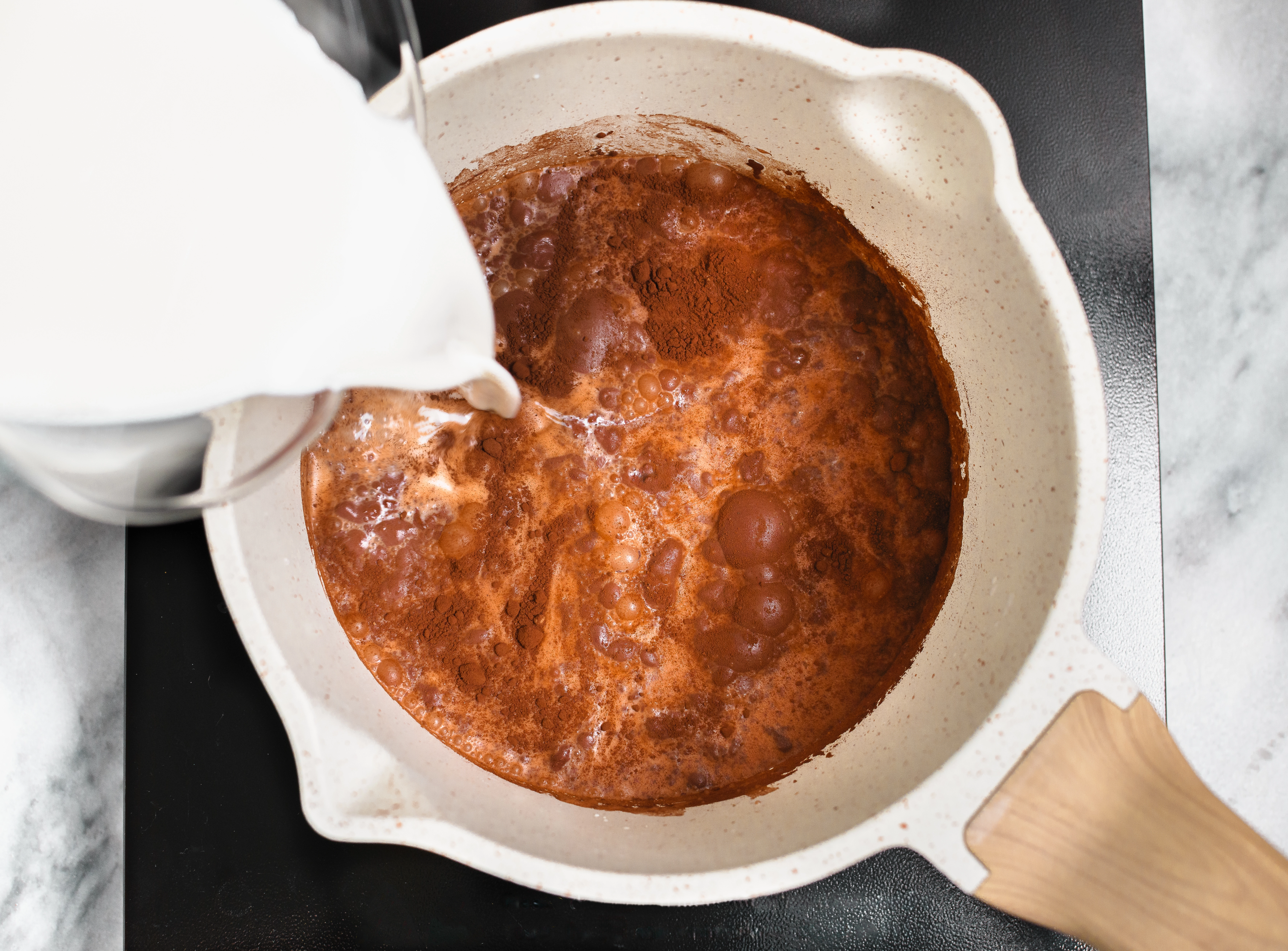 A pot of cocoa powder and milk heating on the stovetop.