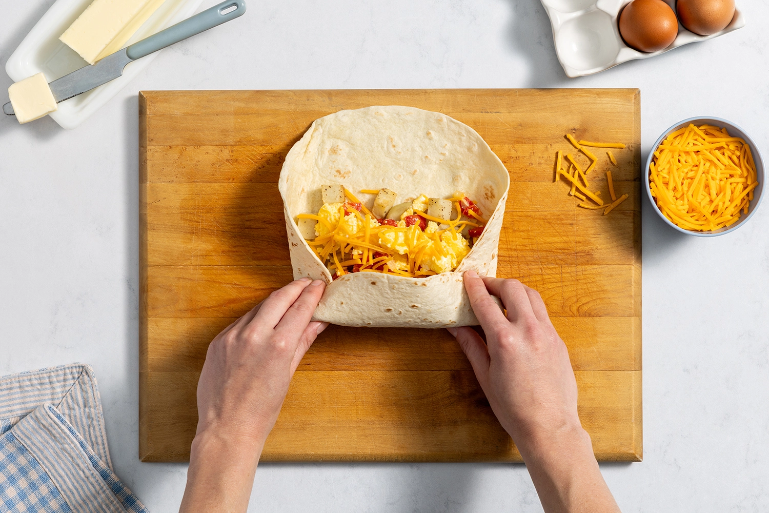 Top-down view of hands folding a flour tortilla filled with scrambled eggs and cheese