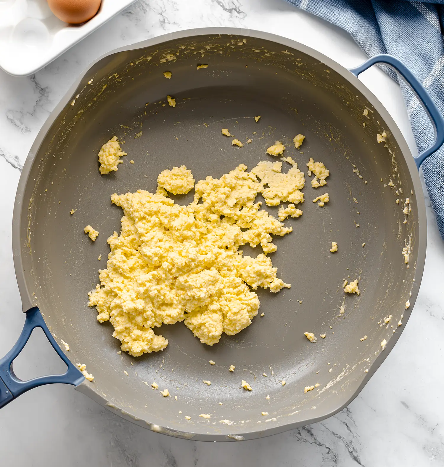 A hot skillet with cooked scrambled eggs on a counter ready to be served.