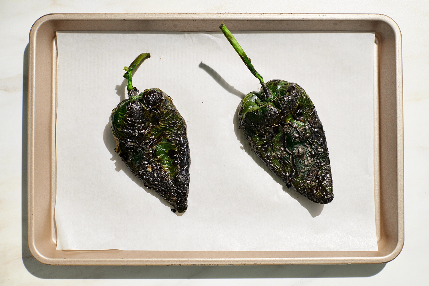 Two roasted poblano peppers on a baking sheet.