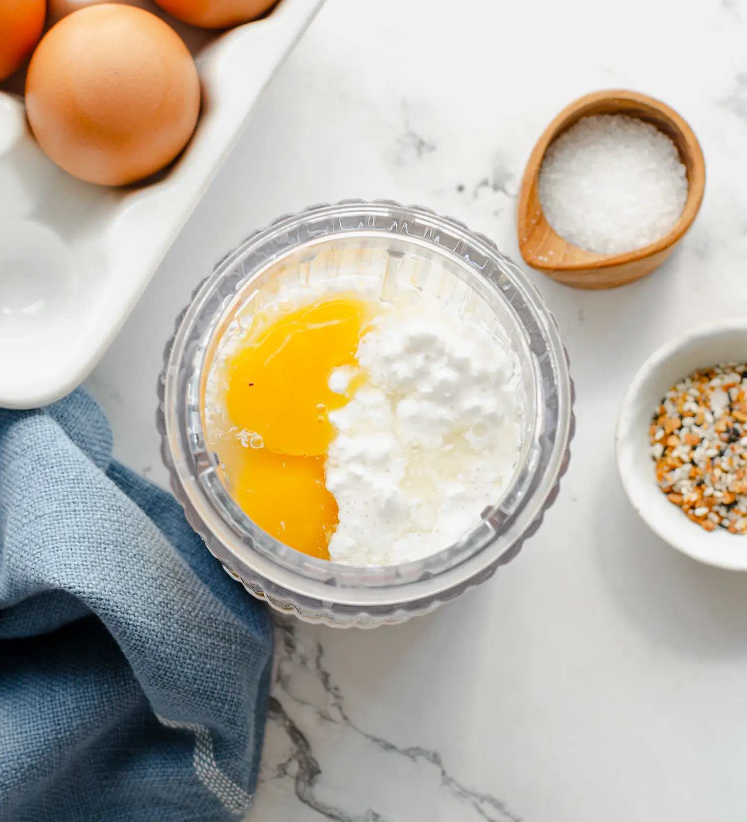 An eggs and cottage cheese mixture in a bowl next to bagel seasoning and salt